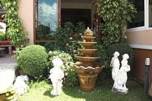 A garden with a tiered water fountain, a spherical hedge, and two white statues. - Baanmalai Hotel Chiangrai (Chiang Rai)