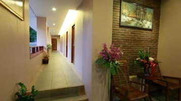 A hotel hallway with a staircase, a reception desk, and a painting on the wall.