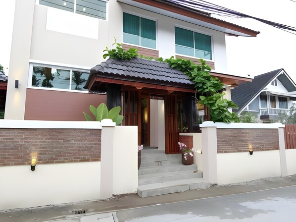 A modern two-story house with a covered entrance, a brick wall, and a small garden area.