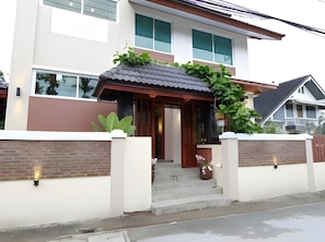 A modern two-story house with a covered entrance, a brick wall, and a small garden area.