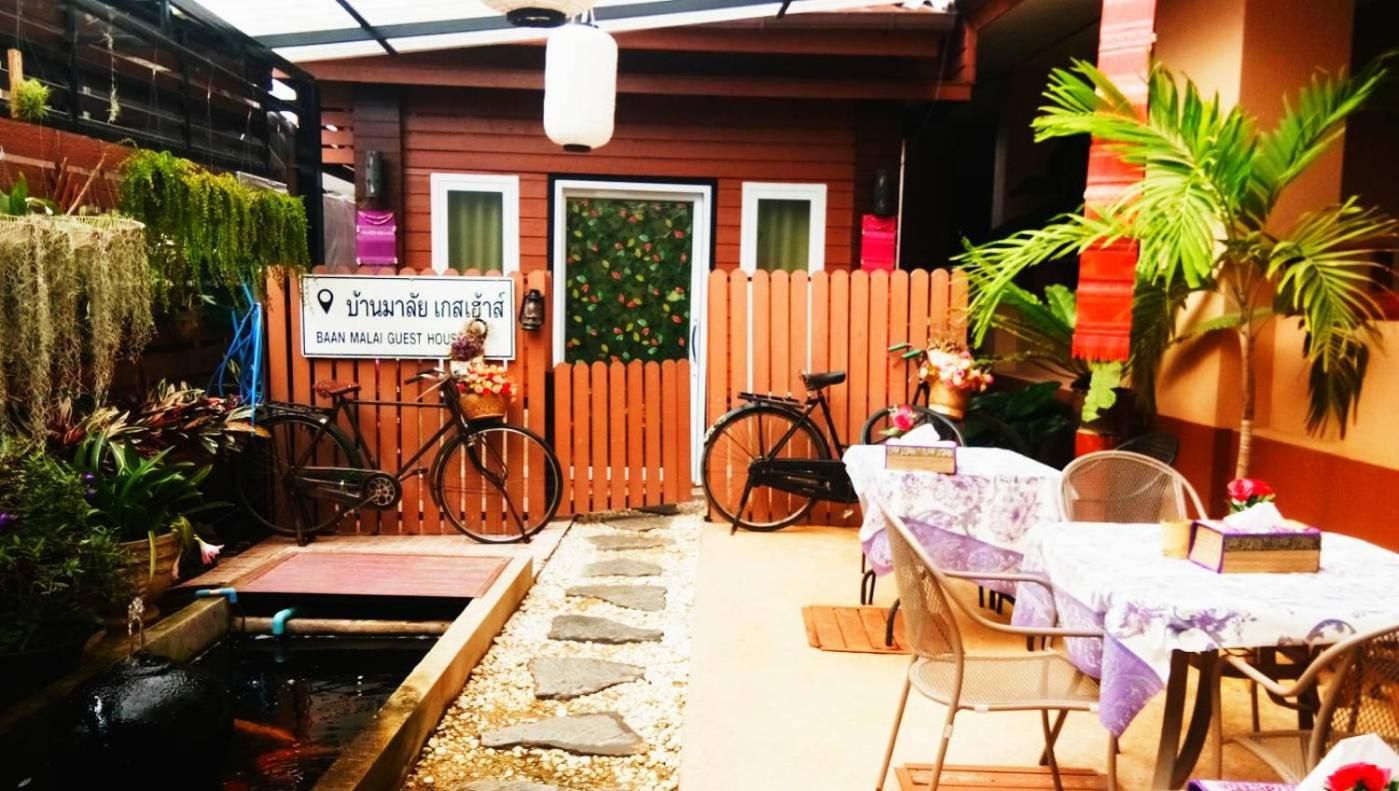 A guest house with a wooden fence, bicycles, a table with a chair, and potted plants.