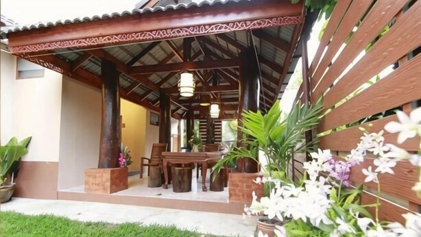A covered outdoor seating area with a table and chairs, surrounded by potted plants and flowers. - Baanmalai Hotel Chiangrai (Chiang Rai)