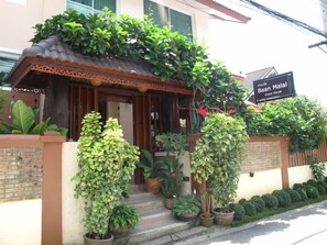 A guest house with a traditional architectural style, featuring a tiled roof and wooden door. There are potted plants and a sign indicating the name of the guest house. - Baanmalai Hotel Chiangrai (Chiang Rai)