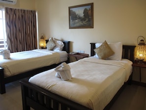 Une chambre d’hôtel avec deux lits, un tableau au mur et une fenêtre avec des rideaux.