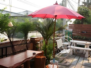 Un espacio al aire libre con mesas y sillas de madera, un paraguas rojo y una planta en maceta.