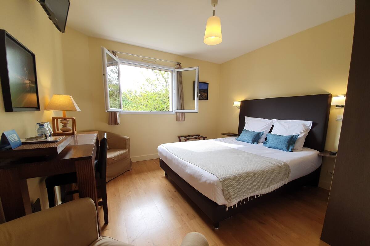 A hotel room with a bed, desk, chair, and a window with curtains.