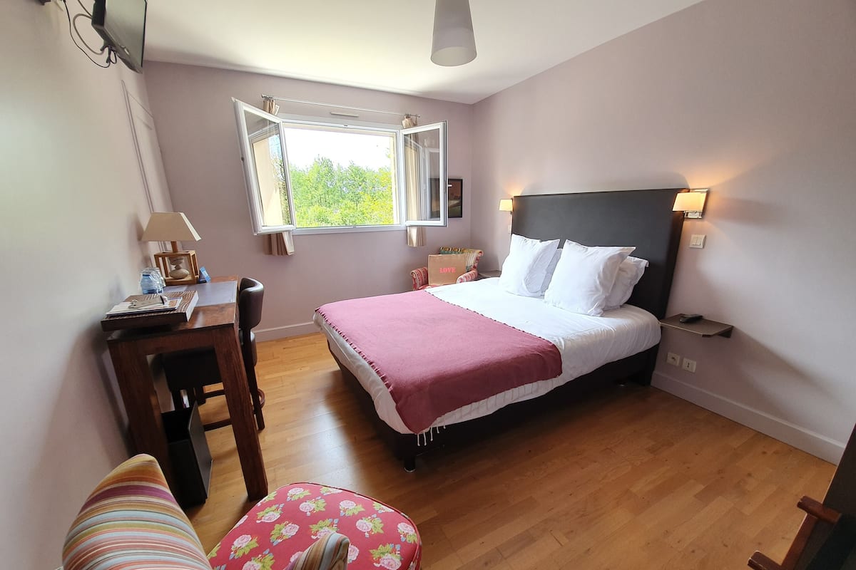 A bedroom with a bed, a desk, a chair, a window, and a lamp.