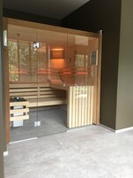 Una sauna moderna con puerta de vidrio, bancos de madera y suelo de baldosas.