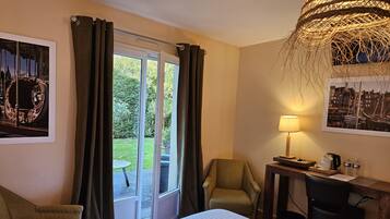 A hotel room with a bed, a desk with a lamp, a chair, and a view of the outdoors through a window.
