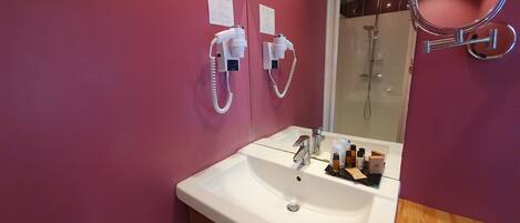 Un baño con lavamanos blanco, espejo, cabezal de ducha de mano y tocador de madera.