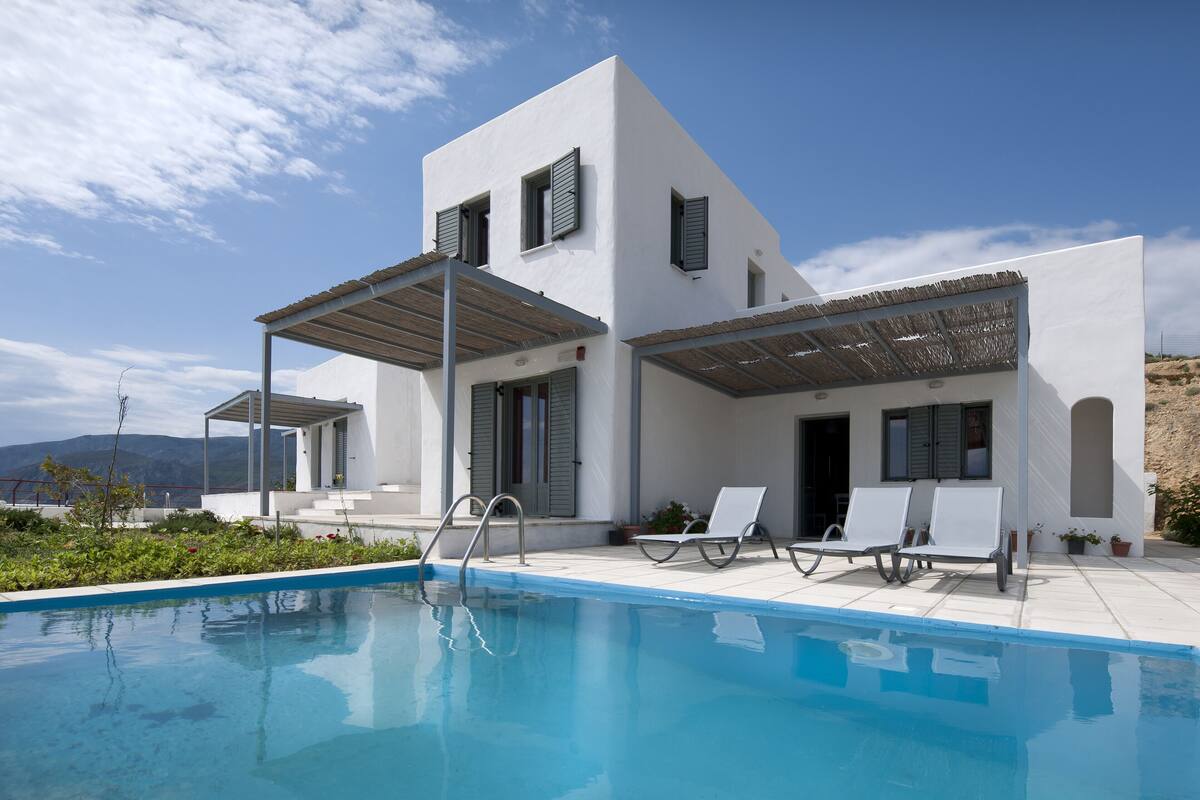 A modern villa with a swimming pool, outdoor seating, and a view of the mountains.
