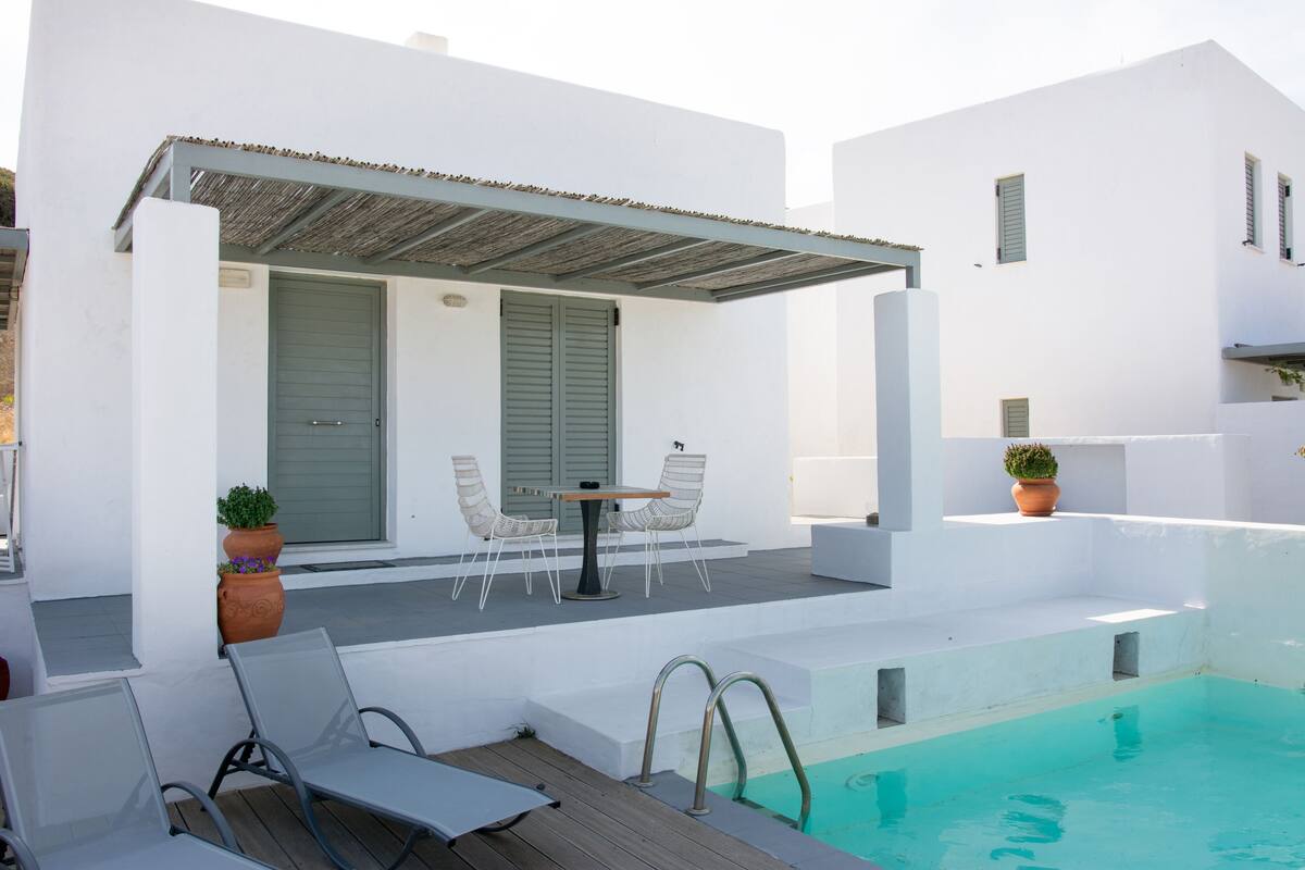 A white building with a pool, outdoor seating, and potted plants.