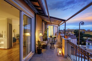 A balcony with a view of the city, furnished with chairs and tables, and potted plants.