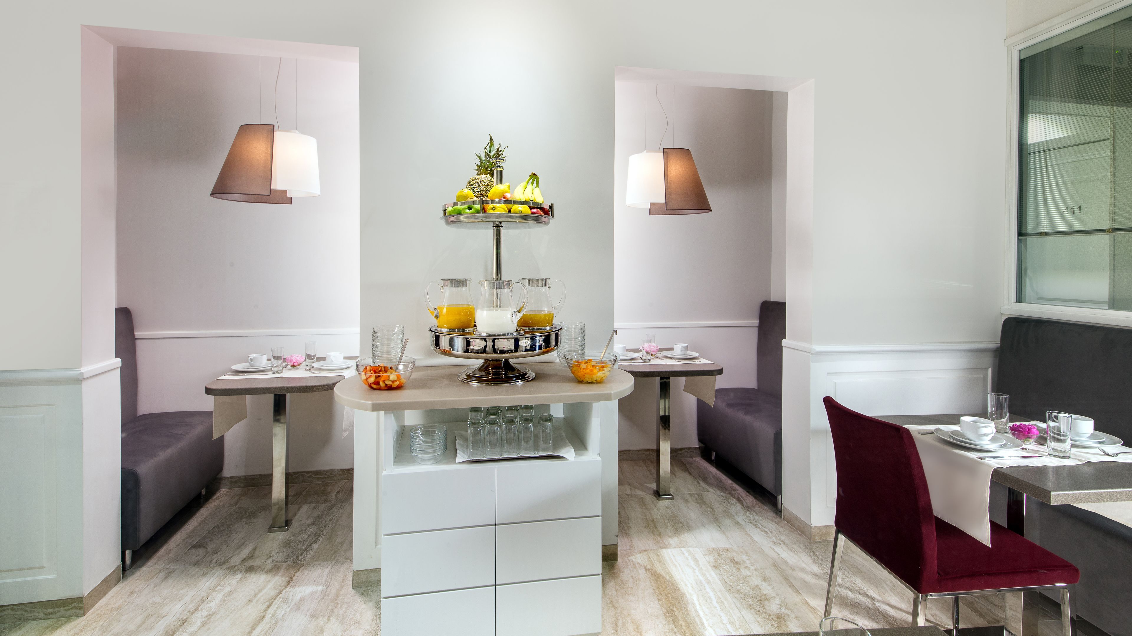 A modern dining area with two tables, each with a chair, a fruit bowl, and a coffee station.