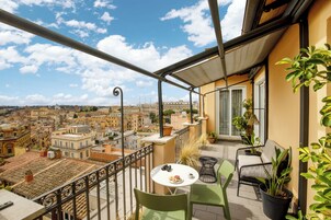 A balcony with a table, chairs, and potted plants.