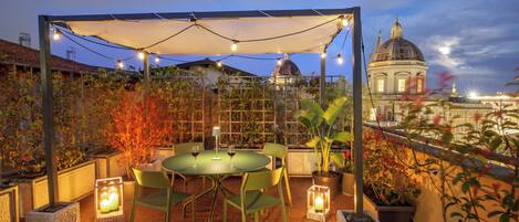 Un patio exterior con mesa y sillas, luces colgantes y plantas en macetas.