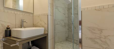 A bathroom with a white sink, marble tiles, a glass-enclosed shower, and a mirror above the sink.