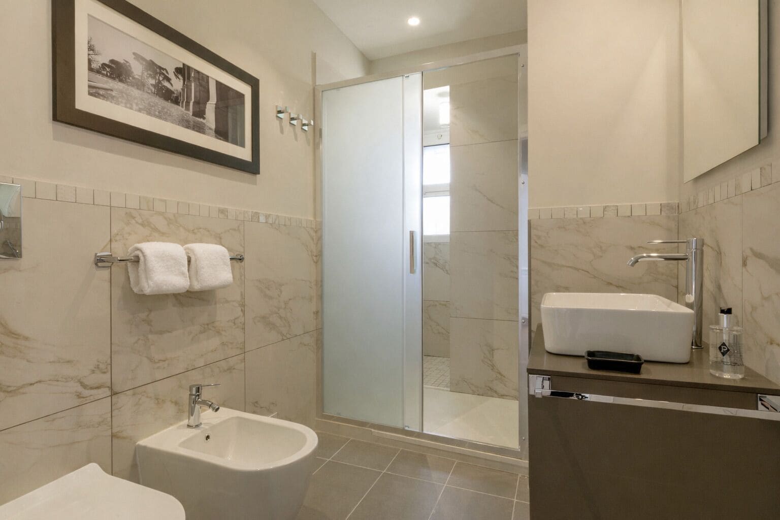 Un baño moderno con bidé, lavamanos y cabina de ducha de vidrio.