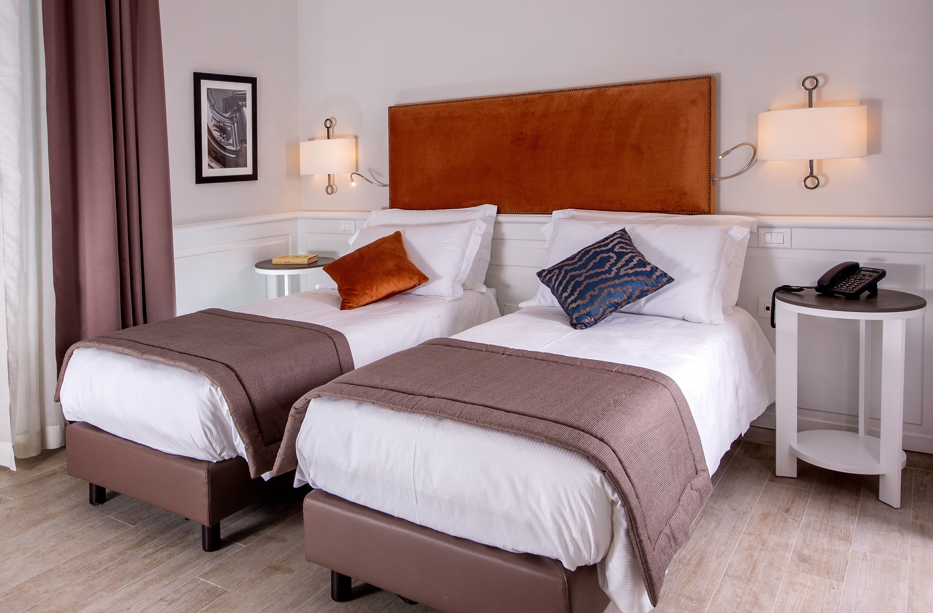 A hotel room with two beds, brown headboards, white bedding, a bedside table with a lamp, and a phone on a side table.