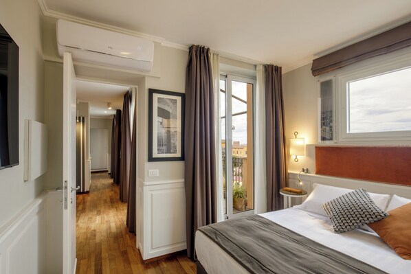 Une chambre d’hôtel comprenant un lit, une table de chevet, une fenêtre avec des rideaux, une porte donnant sur une autre pièce et un couloir.