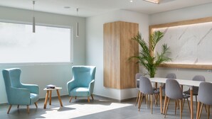 Un comedor moderno con una mesa grande y sillas, dos sillones azules, una pequeña mesa redonda con un libro y una planta en maceta.