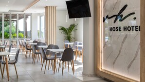 Un moderno vestíbulo de hotel con una gran pantalla de televisión, una mesa de recepción y un comedor con mesas y sillas.