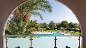 Vista a la piscina con cielo despejado, palmeras y sillones de descanso.