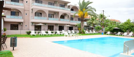A hotel with a swimming pool, outdoor seating, and a palm tree.