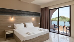 Una habitación de hotel moderna con una cama grande, una mesita de noche y un ventanal corredero que da a un balcón con vistas a un lago y una colina.