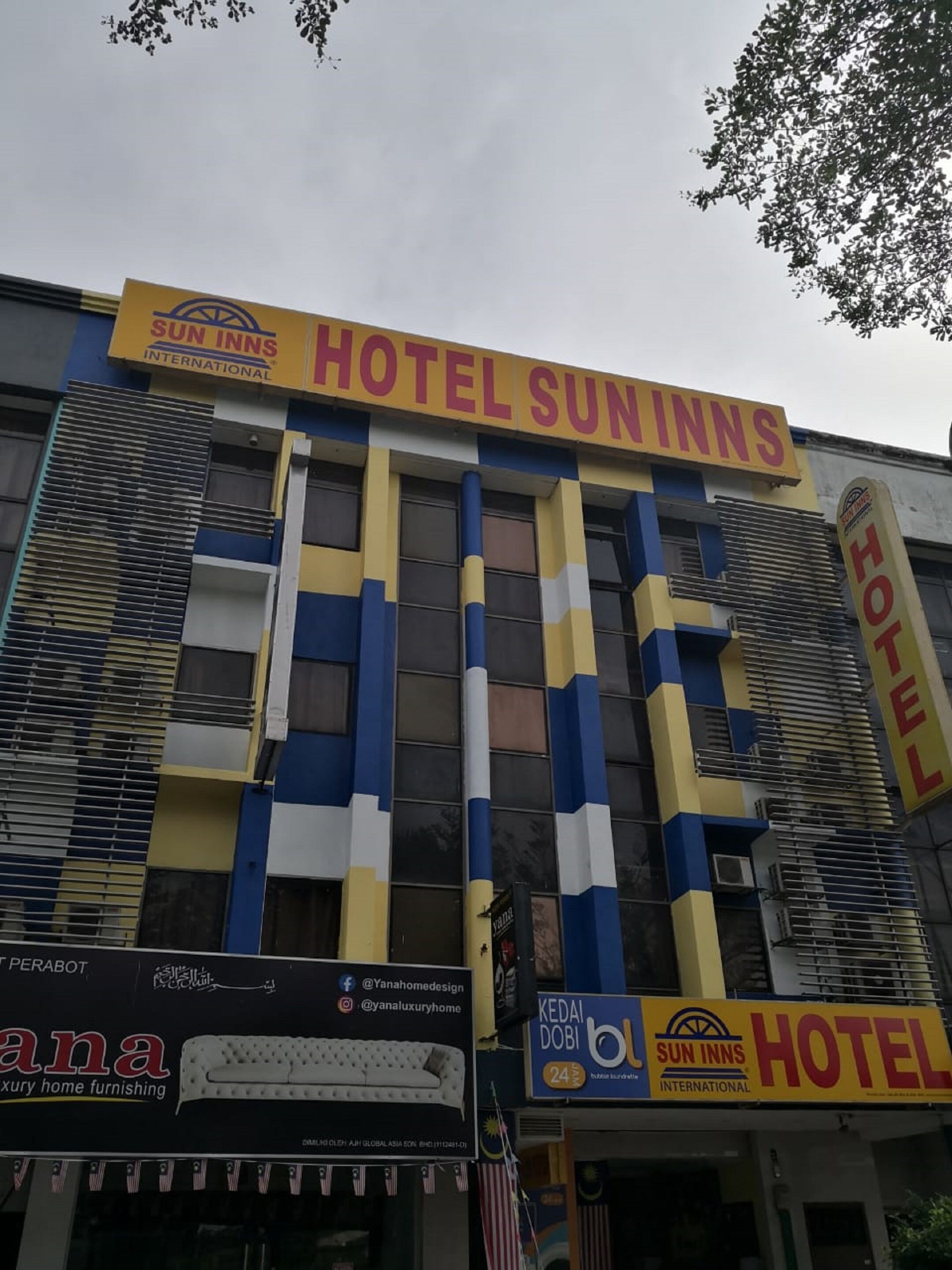 A hotel with a prominent 'HOTEL SUN INNS' sign, featuring a modern design with blue and yellow vertical stripes.