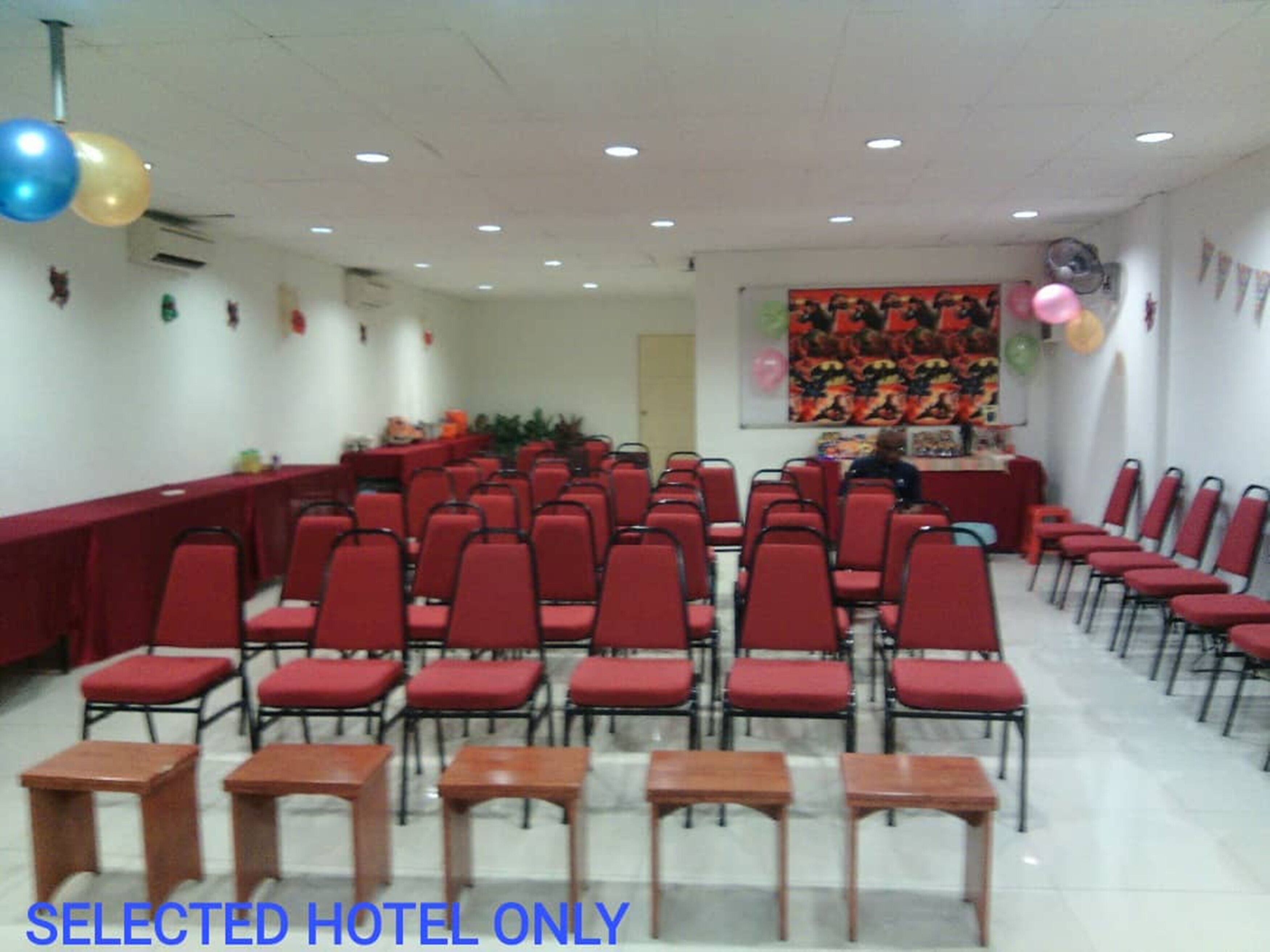 Une salle de conférence avec des rangées de chaises rouges et une longue table, décorée de ballons et ornée d’une fresque colorée sur le mur.