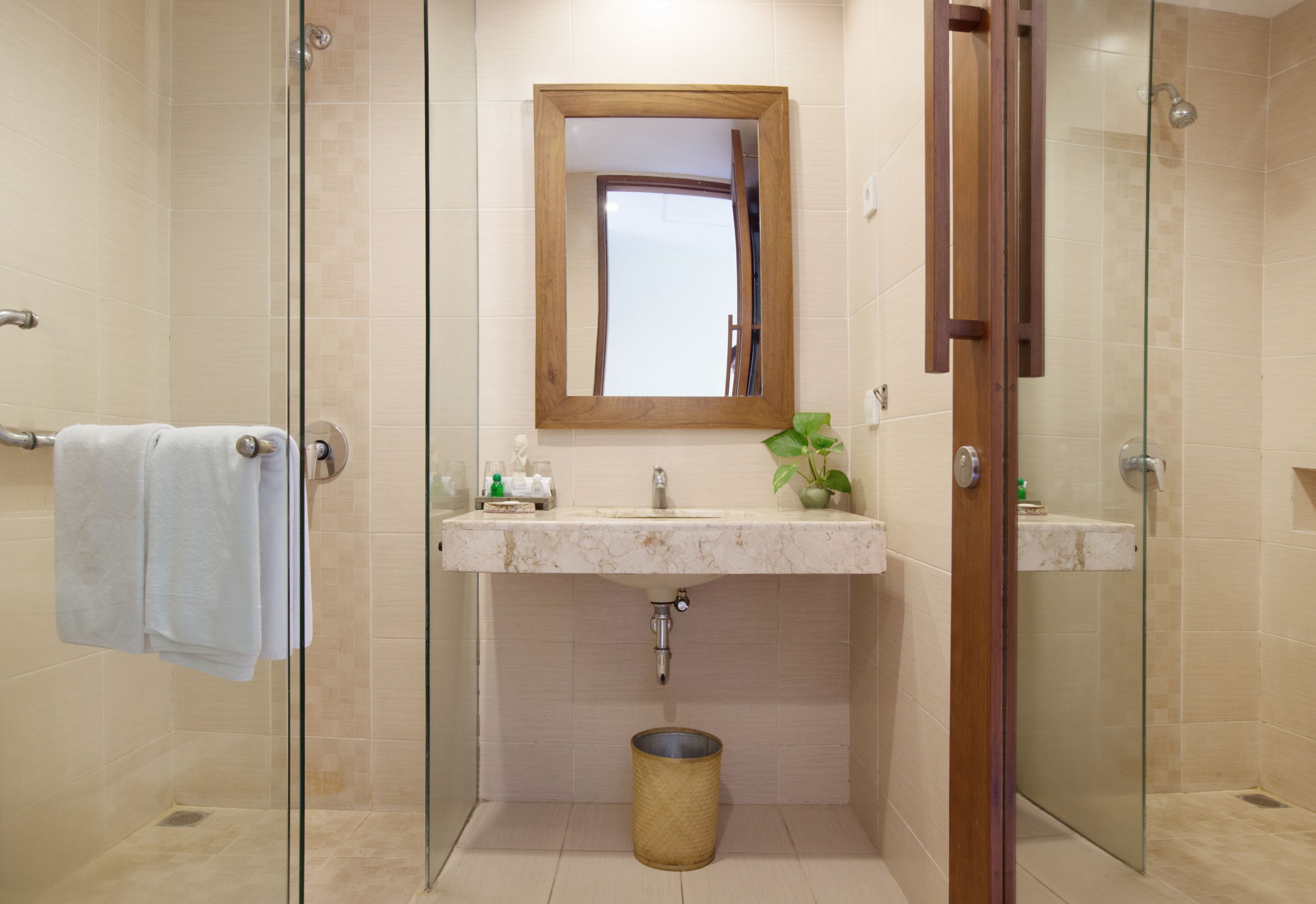 A bathroom with a glass shower enclosure, a wooden-framed mirror, a marble sink, and a potted plant.