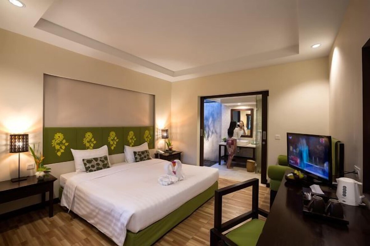 Une chambre d’hôtel avec un grand lit, une télévision, un bureau et une salle de bain visible à travers une porte ouverte.