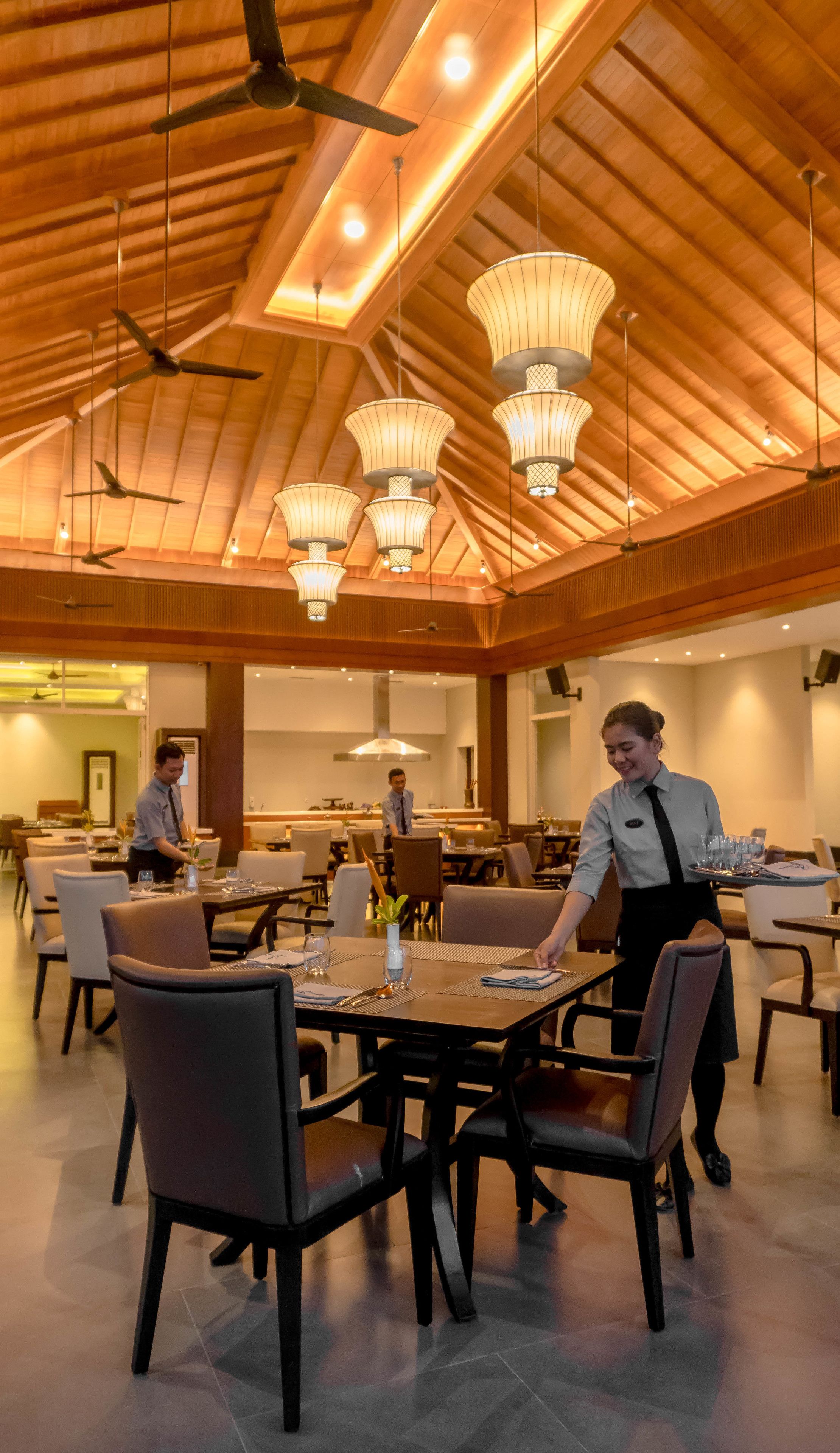 A spacious dining area with multiple tables and chairs, ceiling fans, and pendant lighting.