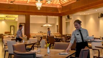 A spacious dining area with multiple tables and chairs, ceiling fans, and pendant lighting.