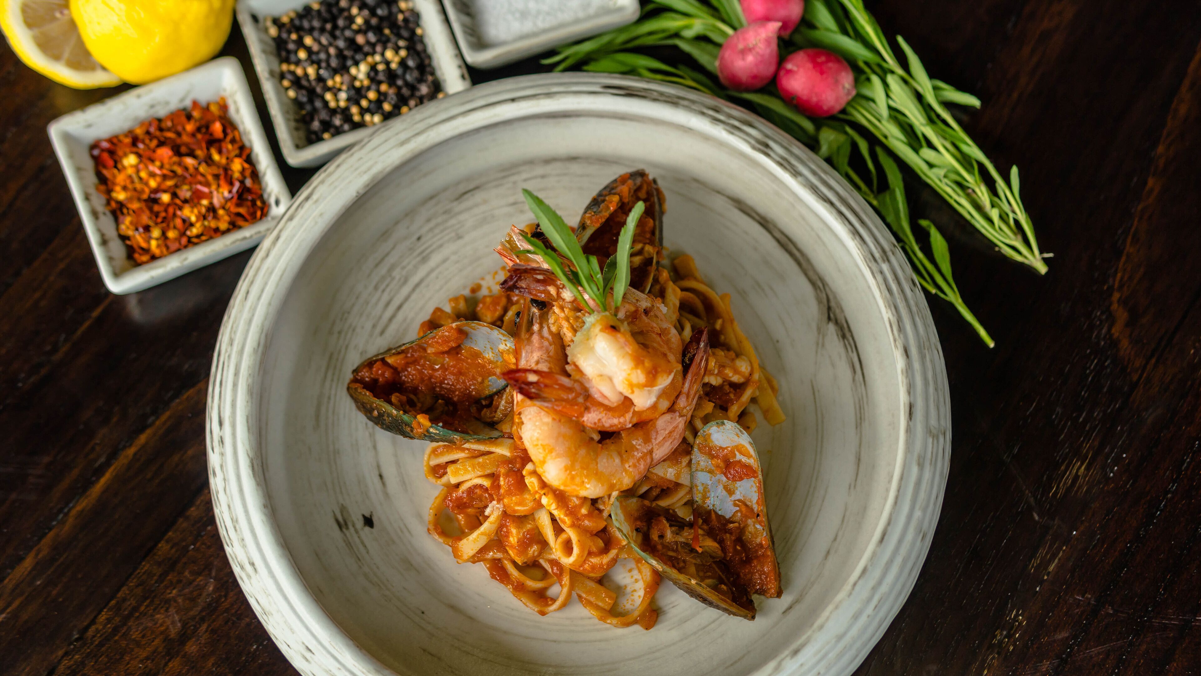 A bowl of pasta with shrimp and a lemon on a wooden table.