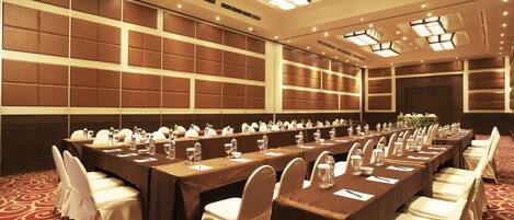 A conference room with long tables, white chairs, and a patterned carpet.