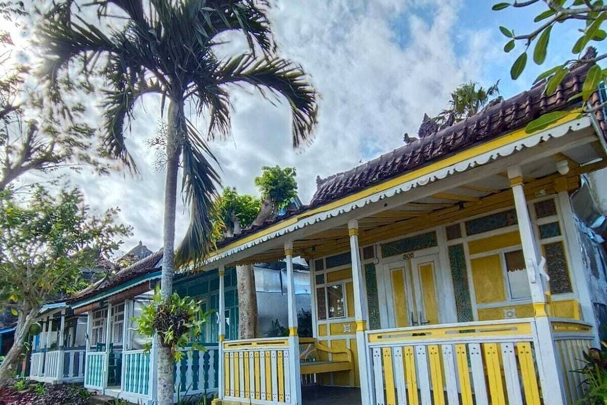 A row of traditional-style buildings with balconies, surrounded by tropical vegetation and a clear sky.