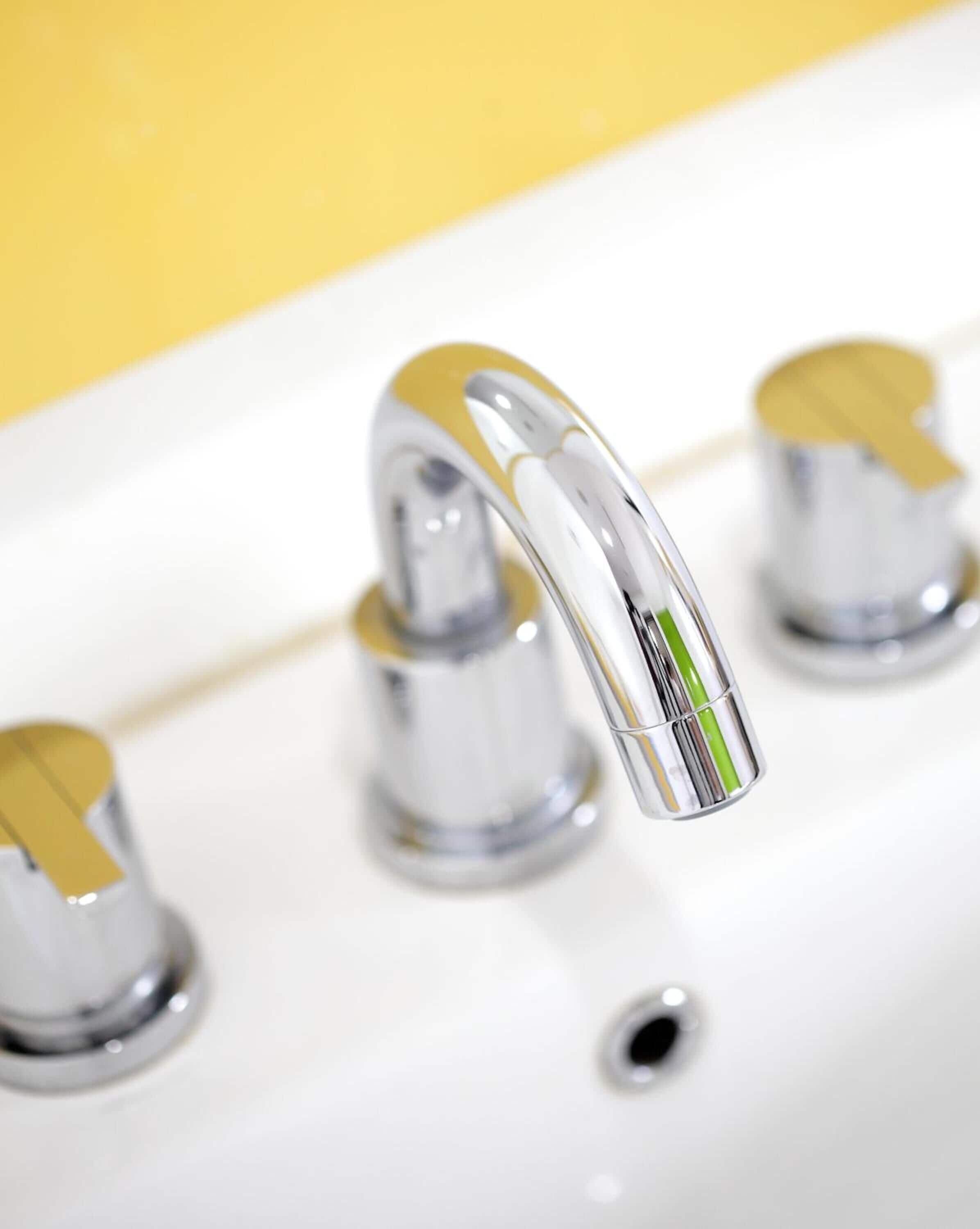A modern bathroom with a chrome faucet and a yellow wall.