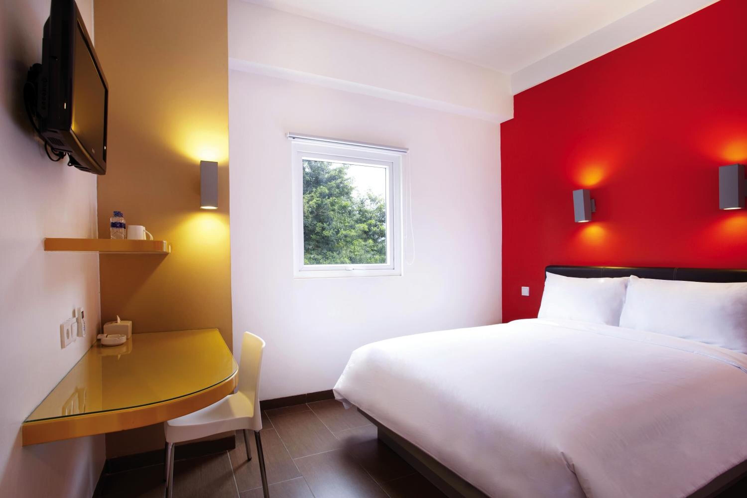 Ein Hotelzimmer mit Bett, Schreibtisch, Sessel, Fernseher und einem Fenster mit Blick auf Grünflächen.