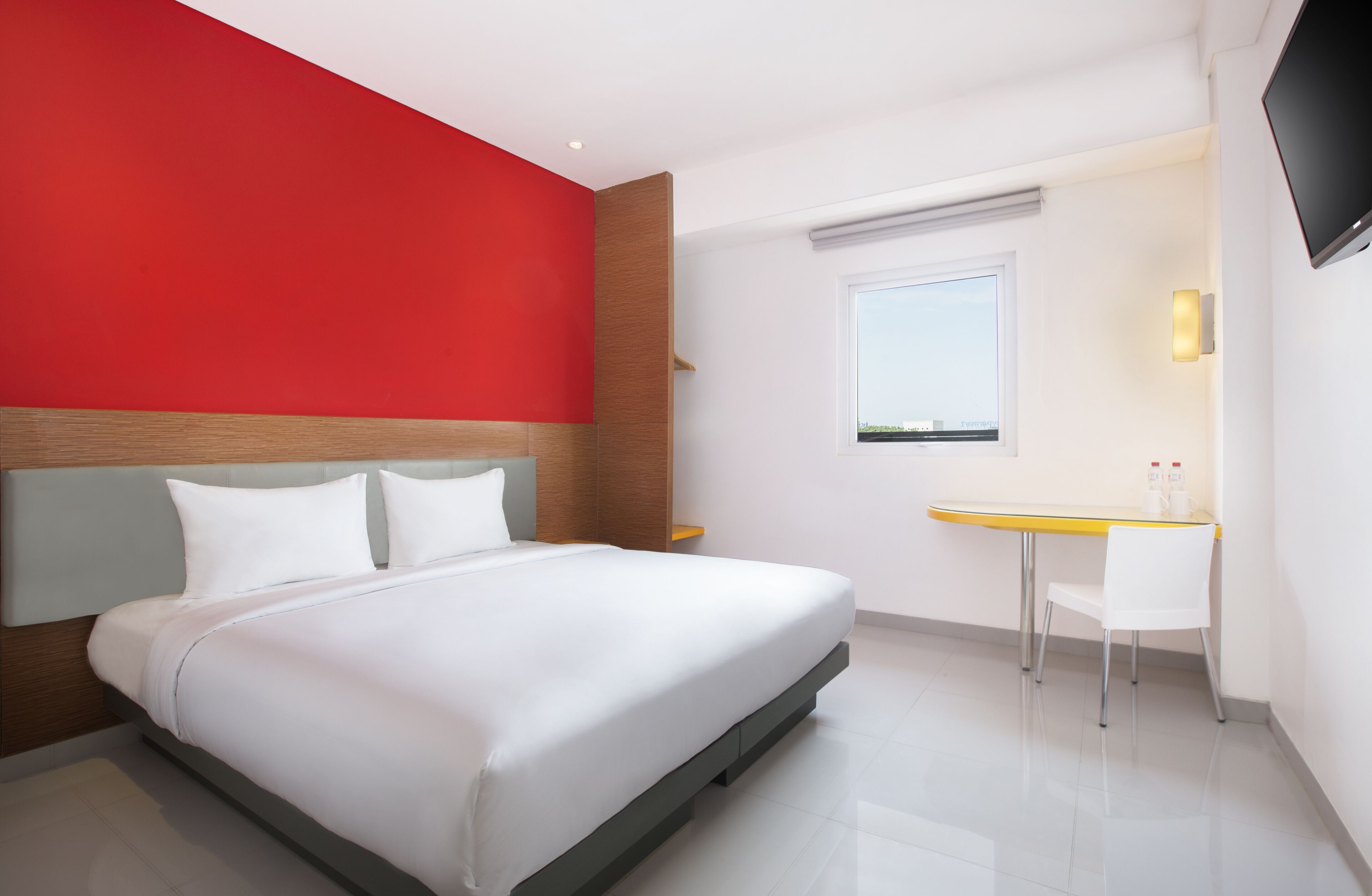 A modern hotel room with a bed, a desk, and a TV.