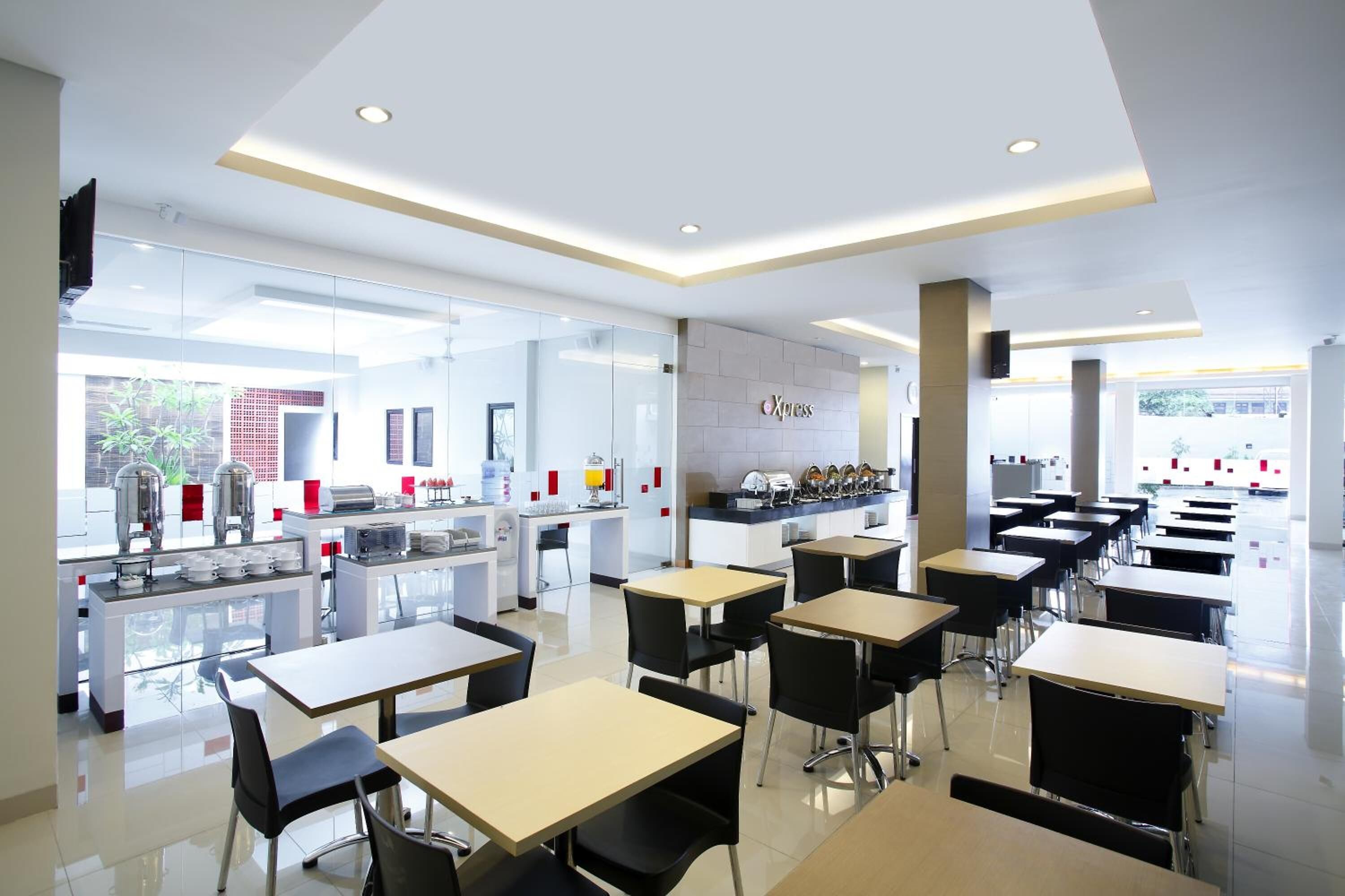 Un espace repas moderne avec des tables et des chaises, un coin cuisine équipé d’appareils électroménagers et un mur sur lequel est inscrit le mot « Xpress ».