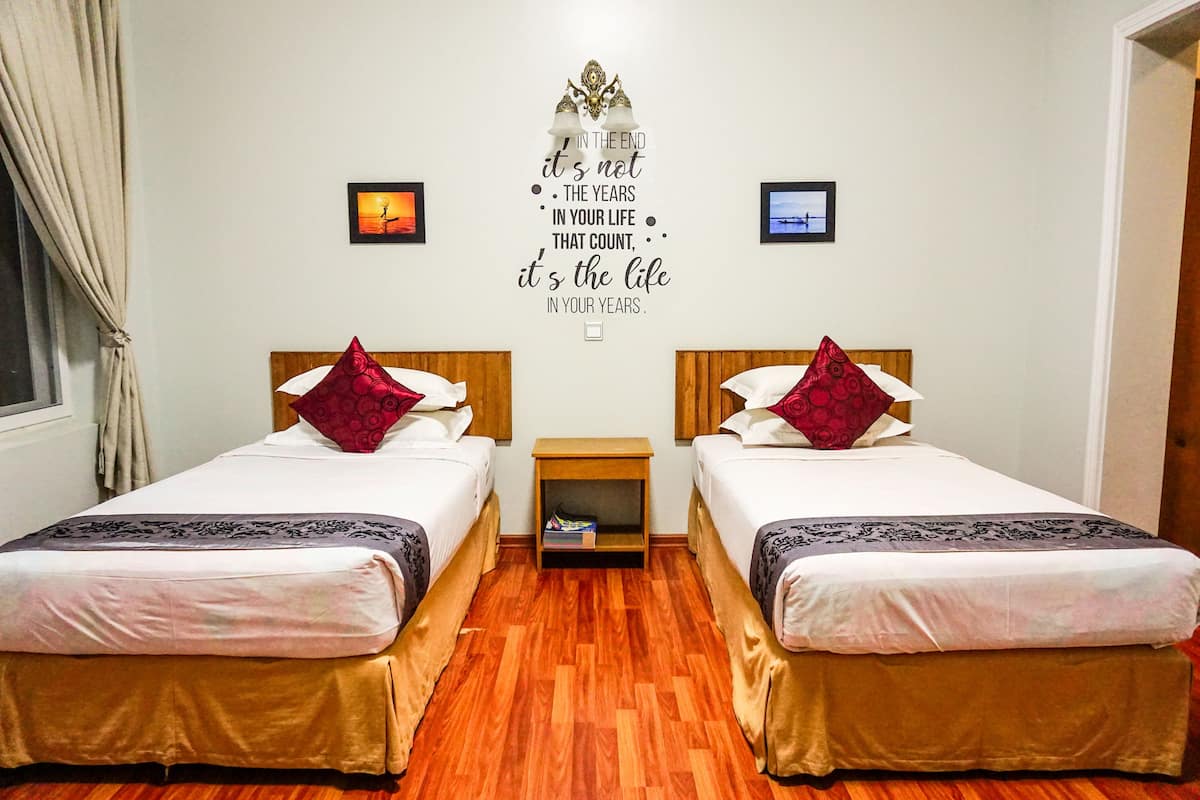 A hotel room with two single beds, a small wooden nightstand, and a motivational quote on the wall.