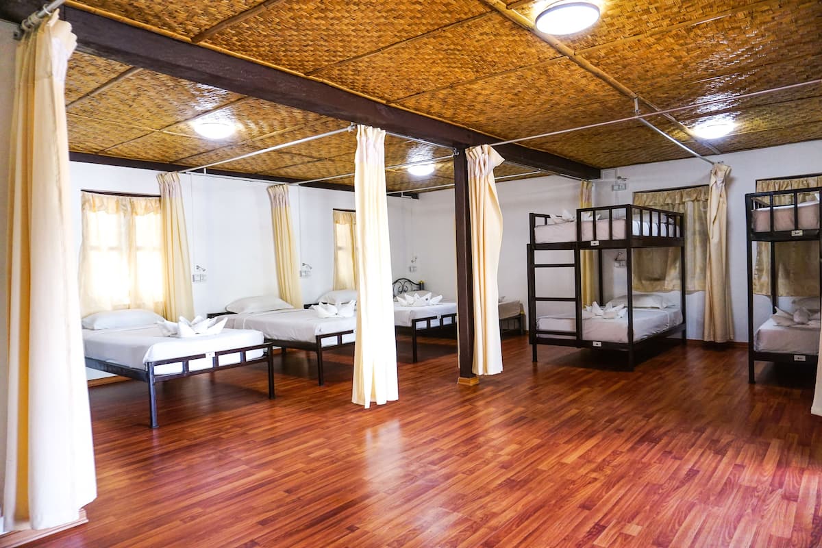 A room with wooden flooring, bunk beds, and curtains.