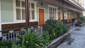 A row of hotel rooms with large windows, a wooden balcony, and a brick wall.
