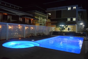 Ein Swimmingpool mit einem runden Whirlpoolbereich, umgeben von einem Zaun und Liegestühlen.