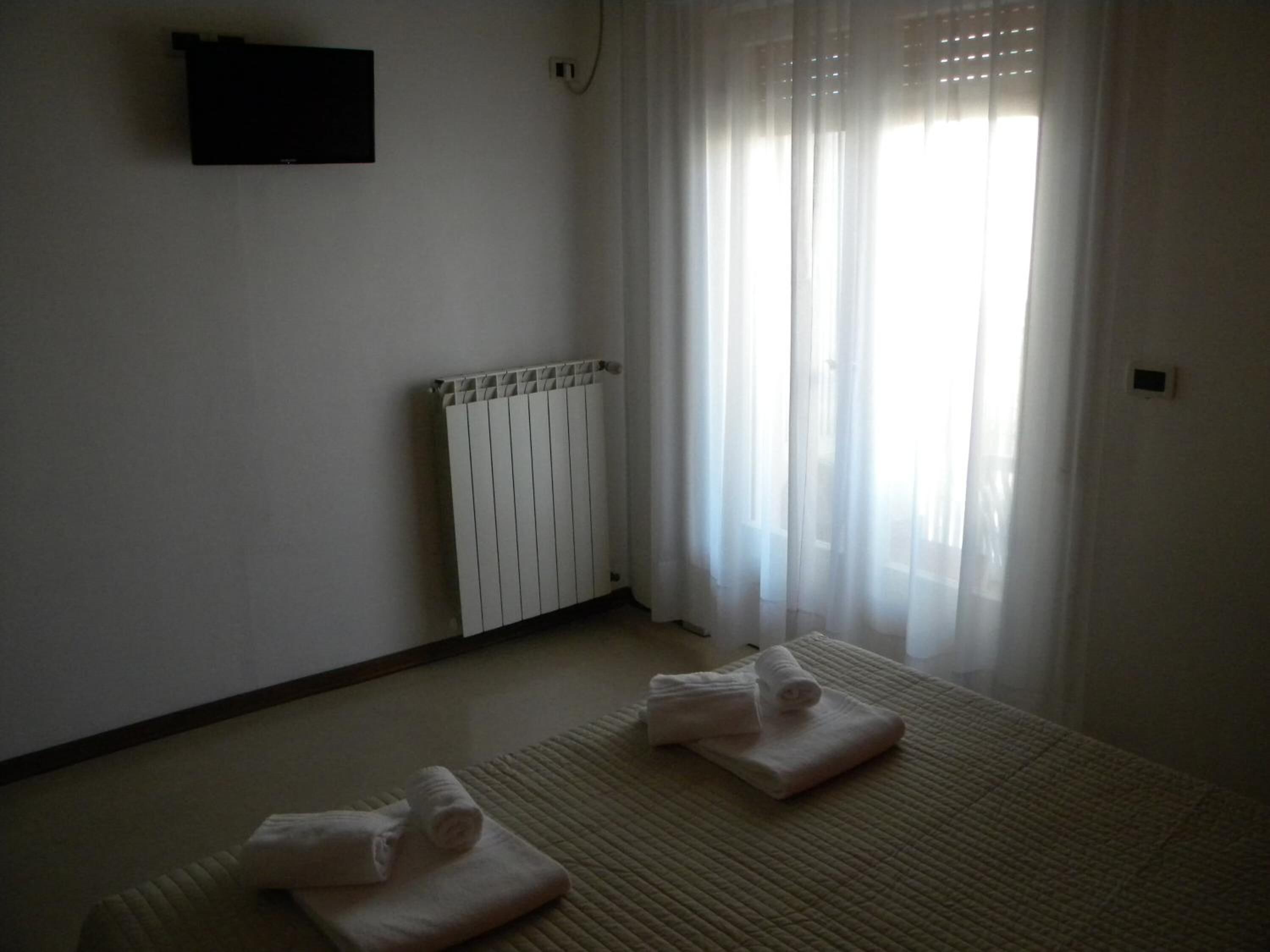 A room with a bed, a radiator, and a window with sheer curtains.