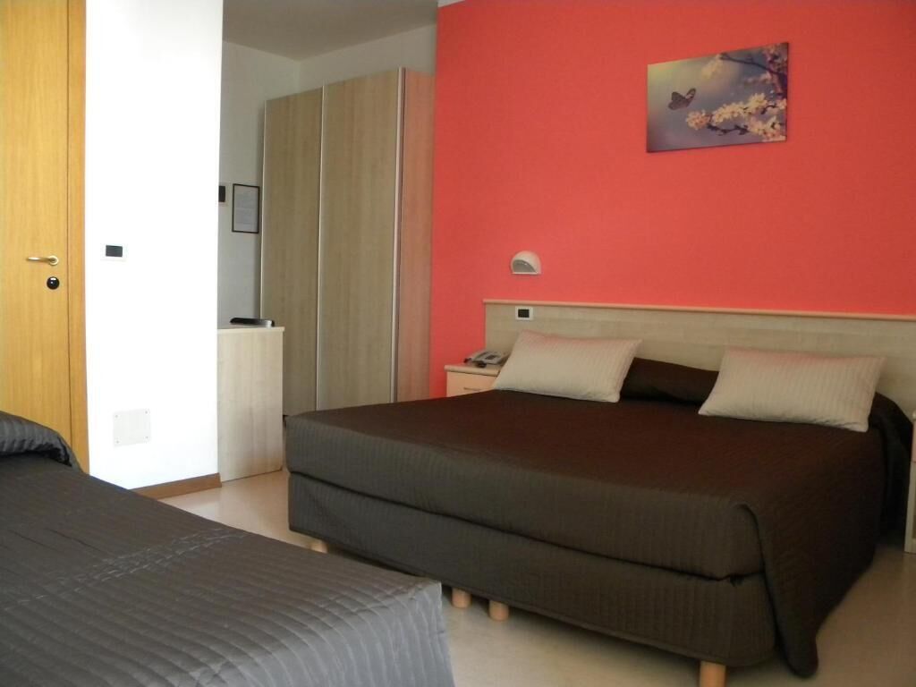A bedroom with a bed, a nightstand, a wall-mounted lamp, and a door.