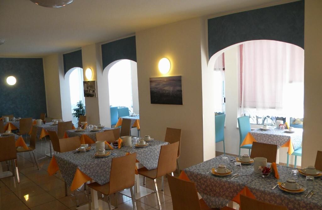 A dining area with tables set for meals, featuring a modern design with orange accents and a view of the outdoors.