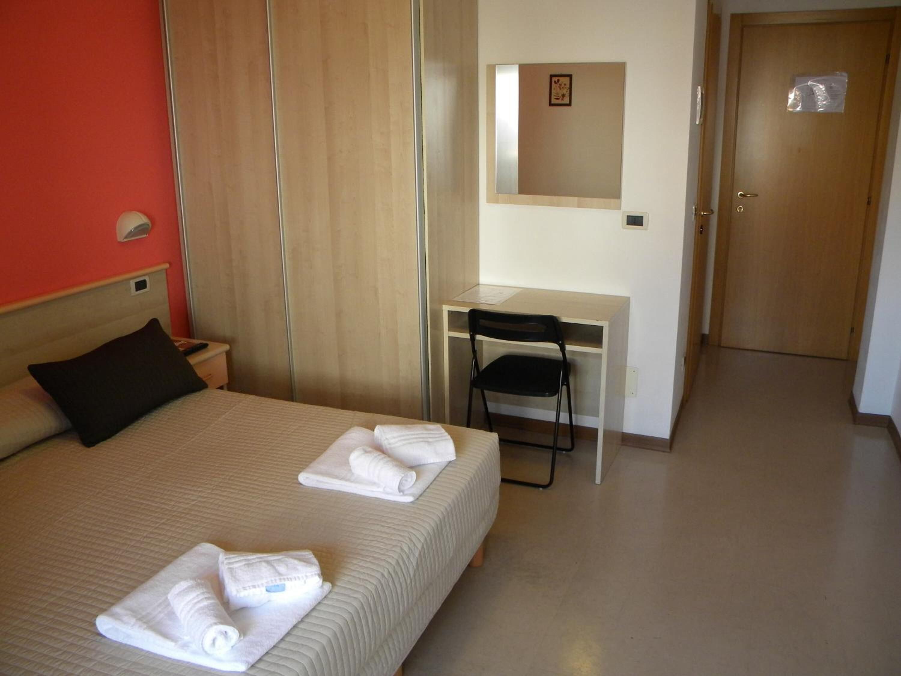 A hotel room with a bed, a desk, a chair, and a door.